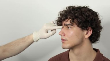 4k video rinoplasti burun ya da burun şeklini değiştirmek ve yaralanmadan kaynaklanan sorunları düzeltmek ya da solunum sorunlarını iyileştirmek için. KBB doktoru burun estetiği ya da septoplasti ameliyatından önce hastaya dokunuyor.