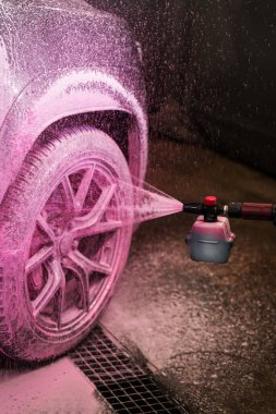 Köpük aplikatör kullanarak arabanın çamurluğuna ve tekerleğine pembe köpük sürme işlemi. Otomobil yıkamada pembe deterjan kullanarak araba yıkamak.