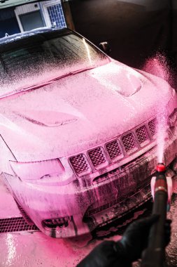Otomobil yıkamada elle yıkama. Aplikatörü kullanarak arabaya pembe köpük sürüyorum. Pembe köpüklü araba temizleme işlemi