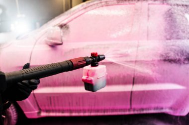 Köpük aplikatörü kullanarak arabanın gövdesine pembe köpük sürme işlemi. Otomobil yıkama servisinde arabaya pembe köpük deterjan sıkmak.