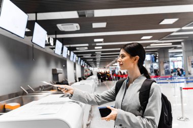 Beyaz bir kadın terminale giriş yapıyor. Havaalanı terminali masasına giriş sırasında bir gezgin belgeleri saklar..