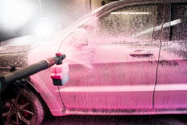 Otomobil yıkama servisindeki arabaya pembe köpük deterjan sıkıyorum. Köpük aplikatörü kullanarak arabanın gövdesine pembe köpük sürme işlemi.