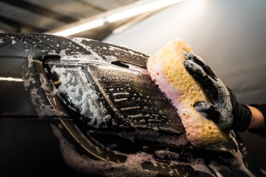 Sünger ve deterjan kullanarak far temizleme işlemi. Otomobil yıkamada yıkanan el yapımı bir araç.