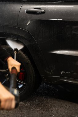 Aracın yüzeyinin derin ve etkili bir şekilde temizlenmesini sağlamak için yüksek basınçlı su akıntıları kullanılıyor. Otomobil yıkama makinesinde araba temizliği. Tekerlek yıkama