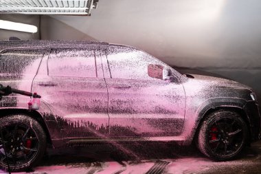 Köpük aplikatörü kullanarak arabanın gövdesine pembe köpük sürme işlemi. Otomobil yıkama servisinde arabaya pembe köpük deterjan sıkmak.