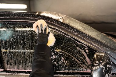 Araba yan camını sünger ve deterjan kullanarak temizleyerek otomatik oto yıkama servisinde araç yıkamak.