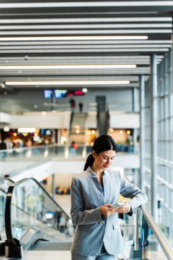 Havaalanı terminalinde akıllı telefonunu kullanarak uçuş numarasını kontrol eden bir kız. Seyahat ve tatil kavramı