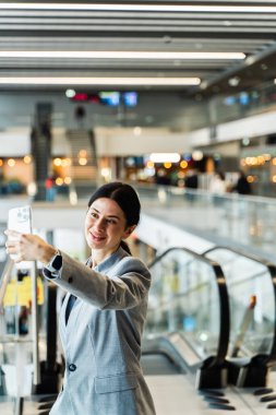 Seyahat blogcusu yolcu beklerken selfie çekiyor. Havaalanı terminalinde selfie çeken Asyalı kadın.