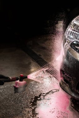 Aplikatörü kullanarak arabaya pembe köpük sürüyorum. Pembe köpüklü araba temizleme işlemi. Otomobil yıkamada elle yıkama.