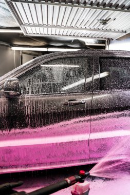 Otomobil yıkama servisindeki arabaya pembe köpük deterjan sıkıyorum. Köpük aplikatörü kullanarak arabanın gövdesine pembe köpük sürme işlemi.