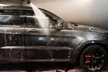Araba yıkama servisinde yüksek basınçlı su jeti ile araba gövdesini temizlemek. Aracın yüzeyindeki köpüğü yıkıyorum.
