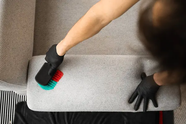 stock image Removing dirt and stains from couch with dry-cleaning brush. Cleaner is brushing off dust from the sofa at home