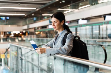 Pasaportu, geçiş kartı ve akıllı telefonu olan bir kadın havaalanı lobisindeki pencerenin yanında duruyor ve kalkışı bekliyor. Havaalanındaki turist panoramik pencerenin yanında güvenlik kontrolü için bekliyor