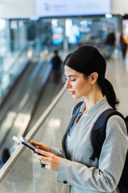 Havaalanı terminalinde akıllı telefonunu kullanarak uçuş numarasını kontrol eden bir kız. Seyahat ve tatil kavramı