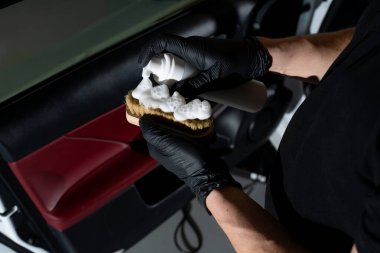 Detaylı fırçada köpüklenme. Arabanın kapı panelini silmek için el temizleme solüsyonu fincanı sıçratır. Ayrıntılı süreç