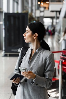 Bagajlı Asyalı gezgin kız biniş kapısına doğru gidiyor. Sırt çantası ve akıllı telefonu olan bir iş kadını kalkışı bekliyor.