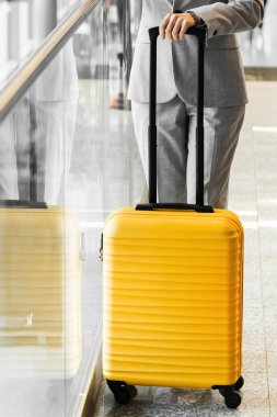 Havaalanı lobisinde sarı bir valiz var. Kadının elinde seyahat için giysi taşıyan sarı bir valiz var. Seyahat ve tatil kavramı