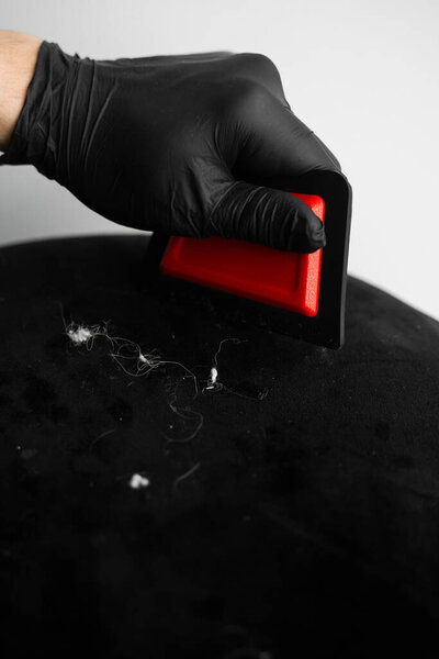 Using the upholstery brush to dry clean furniture from dirt and pet footprints. Cleaner is removing dog hair from an ottoman chair with a fur brush