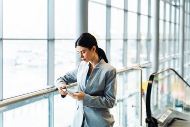 Havaalanı terminalinde akıllı telefonunu kullanarak uçuş numarasını kontrol eden bir kız. Seyahat ve tatil kavramı