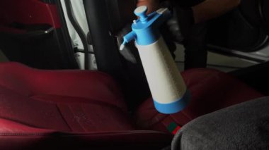 Araba koltuğuna dezenfektan sıçratma 4K video işlemi. Oto koltukları özel deterjan spreyi kullanılarak detaylandırılıyor
