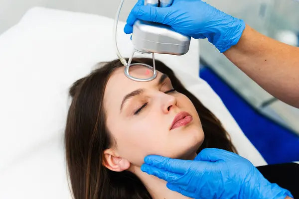 Stock image Process of facial CO2 laser resurfacing. Cosmetologist removes wrinkles and scars using laser from face of attractive girl