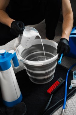 Pouring oxygen bleach mixture in the bucket for cleaning living room furniture. Removing stains and brightening up white furniture with oxygen bleach clipart