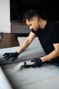 Döşeme mobilyalarını toz ve lekelerden temizlemek için sökücü kullanıyor. Temizlikçi, deterjanlı sökücü kullanarak kanepeyi temizler.