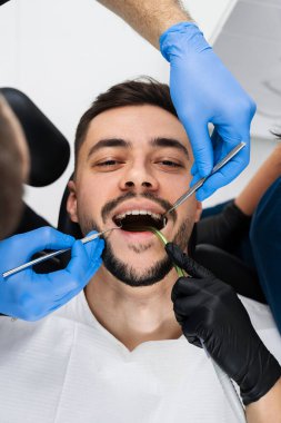 Yakışıklı adam klinikte önleyici diş kontrolü yaptırıyor. Bir dişçi tarafından hastaların ağız boşluğuna yapılan ilk muayene.