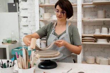 Kız kilden yuvarlak bir şekil alıyor. Keskin bir çömlek bıçağı kullanarak kilden mükemmel yuvarlak bir şekil çıkarmışlar. Seramik sınıfı.