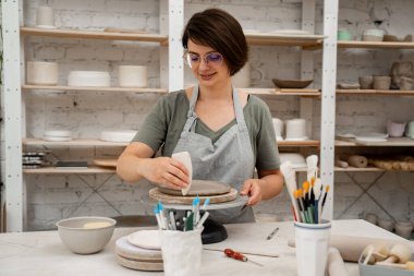 Yumuşak açılı dönüşüm ve kilden bir çömlek kazıyıcıyla kıvrımlı kaburgalar. Kız, kilden bir ürünün kenarlarını yumuşatmak için çömlekçi kullanıyor.