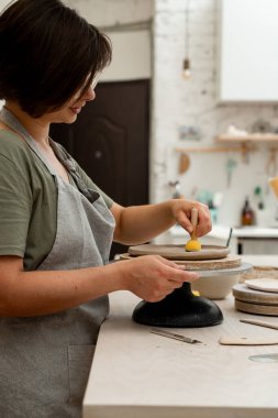 Çömlek atölyesinde kil ürününün yüzeyini pürüzsüz hale getirmek için ahşap saplı sünger kullanmak. Çömleği şekillendirmek ve kilden fazla su emmek için çubuğun üzerinde süngerle çalışmak