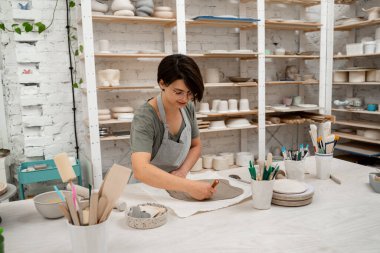 Kız, kil parçasını kesmek için keskin bir kil kesici kullanıyor. Bir yontma aracıyla düz bir kil tabakasından figürler kesmek