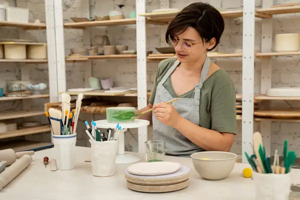 stock image Using a brush to paint a ceramics bowl. Learning how to paint a handmade pottery project. Girl is decorating a clay product with bright green color