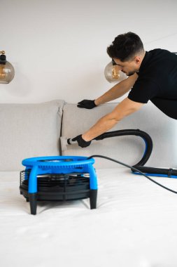 Temizlikçi kanepe yastıklarını sökücüyle yıkıyor ve yatağın yumuşak döşemelerini kurutuyor. Ev mobilyalarını sökücüyle kuru temizleme. Yataktaki ıslak noktaları temizlemek için kurutucu kullanılıyor.