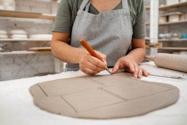 Kız çömlekçiliğe şekil vermek için kil kesici kullanıyor. Dikdörtgen şekilli şekilli bir bıçakla düz bir kil tabakasından şekiller kesiyor.