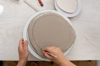 Kız kilden yuvarlak bir şekil alıyor. Keskin bir çömlek bıçağı kullanarak kilden mükemmel yuvarlak bir şekil çıkarmışlar. Seramik sınıfı.