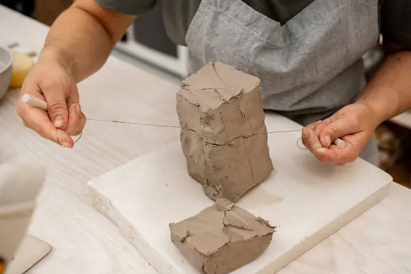 stock image Slicing off a chunk of clay from a large block using a sharp wire clay cutter. Using a wire cutter to cut off a piece of clay before modeling the product