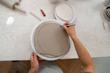 Kız kilden yuvarlak bir şekil alıyor. Keskin bir çömlek bıçağı kullanarak kilden mükemmel yuvarlak bir şekil çıkarmışlar. Seramik sınıfı.