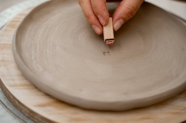 Çömlekçilik projesine harf ve süs kazımak için kil krampı kullanmak. Seramik atölyesinde kil ürünleri özel paternlerle ve sembollerle dekore etmek