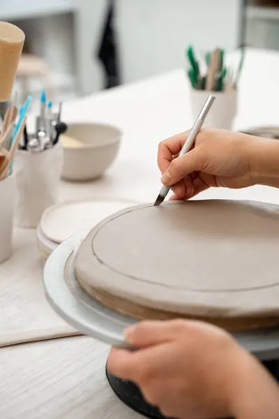 stock image Girl is modeling clay into a round form. Using a sharp pottery carving knife to cut out a perfect round shape from clay. Ceramics class