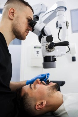Diş hekimi dijital mikroskobu çalışıyor. Dişçi hastanın dişlerini parlatmak için ameliyat mikroskobu kullanıyor.