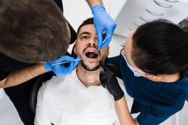 Bir dişçi tarafından hastaların ağız boşluklarının ilk muayenesi. Yakışıklı adam klinikte önleyici diş kontrolü yaptırıyor.