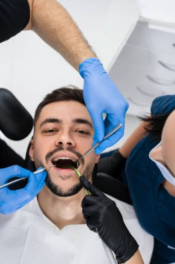 Bir dişçi tarafından hastaların ağız boşluklarının ilk muayenesi. Yakışıklı adam klinikte önleyici diş kontrolü yaptırıyor.