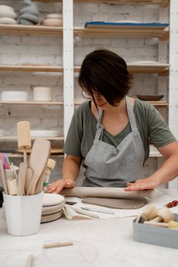 Preparing clay for cutting and assembling it. Slab building method in ceramics crafting. Using a wooden stick to roll out a flat sheet of clay clipart