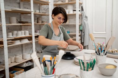 Kız kilden yuvarlak bir şekil alıyor. Keskin bir çömlek bıçağı kullanarak kilden mükemmel yuvarlak bir şekil çıkarmışlar. Seramik sınıfı.