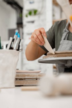 Yumuşak açılı dönüşüm ve kilden bir çömlek kazıyıcıyla kıvrımlı kaburgalar. Kız, kilden bir ürünün kenarlarını yumuşatmak için çömlekçi kullanıyor.