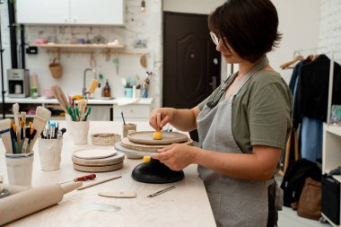 Kız çömleği şekillendirmek ve kilden fazla su emmek için çubuğun üzerinde süngerle çalışıyor. Bir çömlek atölyesinde kil ürününün yüzeyini pürüzsüz hale getirmek için ahşap saplı sünger kullanmak.