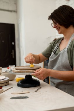 Kız çömleği şekillendirmek ve kilden fazla su emmek için çubuğun üzerinde süngerle çalışıyor. Bir çömlek atölyesinde kil ürününün yüzeyini pürüzsüz hale getirmek için ahşap saplı sünger kullanmak.