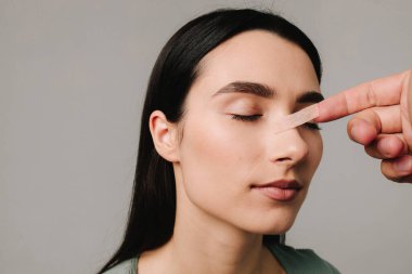 Burun estetiği. Estetik cerrah burun buruna burun bandı takıyor. Şeklini korumak için burun üstüne bandaj uygulamak, şişkinliği azaltmak ve görünümü iyileştirmek
