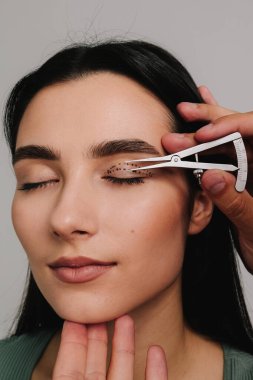 Göz kapaklarını düzeltmek için birofaroplasti hazırlıyorum. Üst blefaroplasti. Plastik cerrah, Castroviejo kalibreli hastasının gözünün içindeki cerrahi mesafeyi ölçüyor.